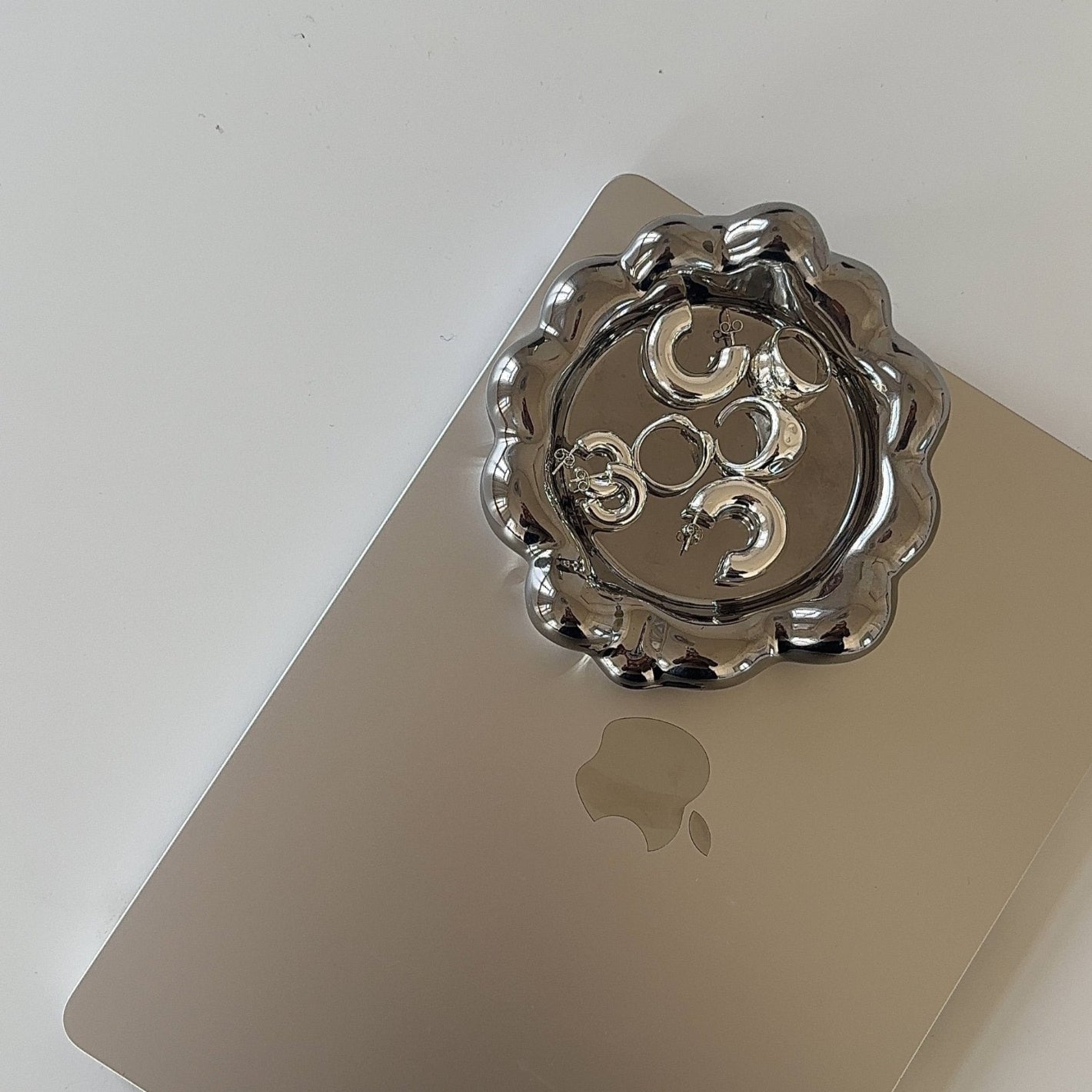 bold silver jewelry pieces in shiny jewelry tray on MacBook on white desk