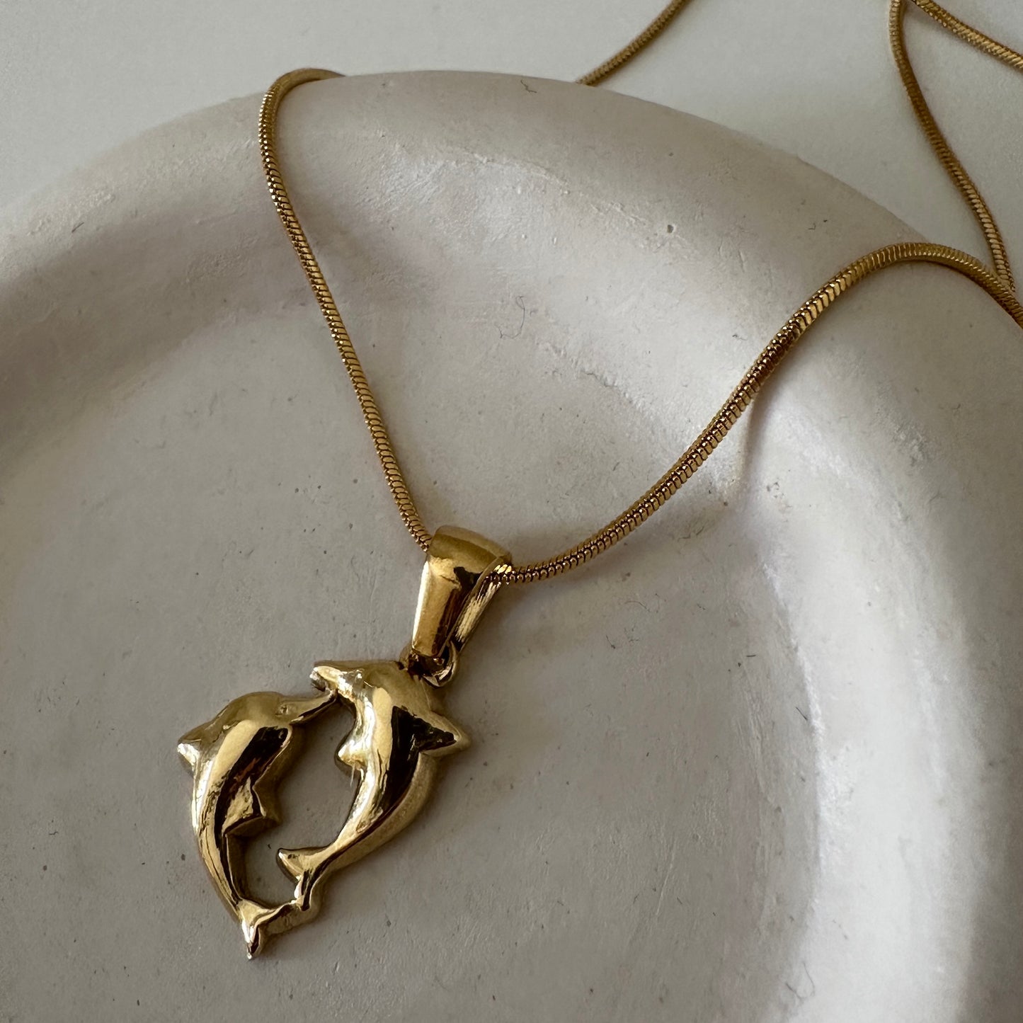 Dancing Dolphins Delfin Kette in gold in Nahaufnahme auf weißer Keramikschale