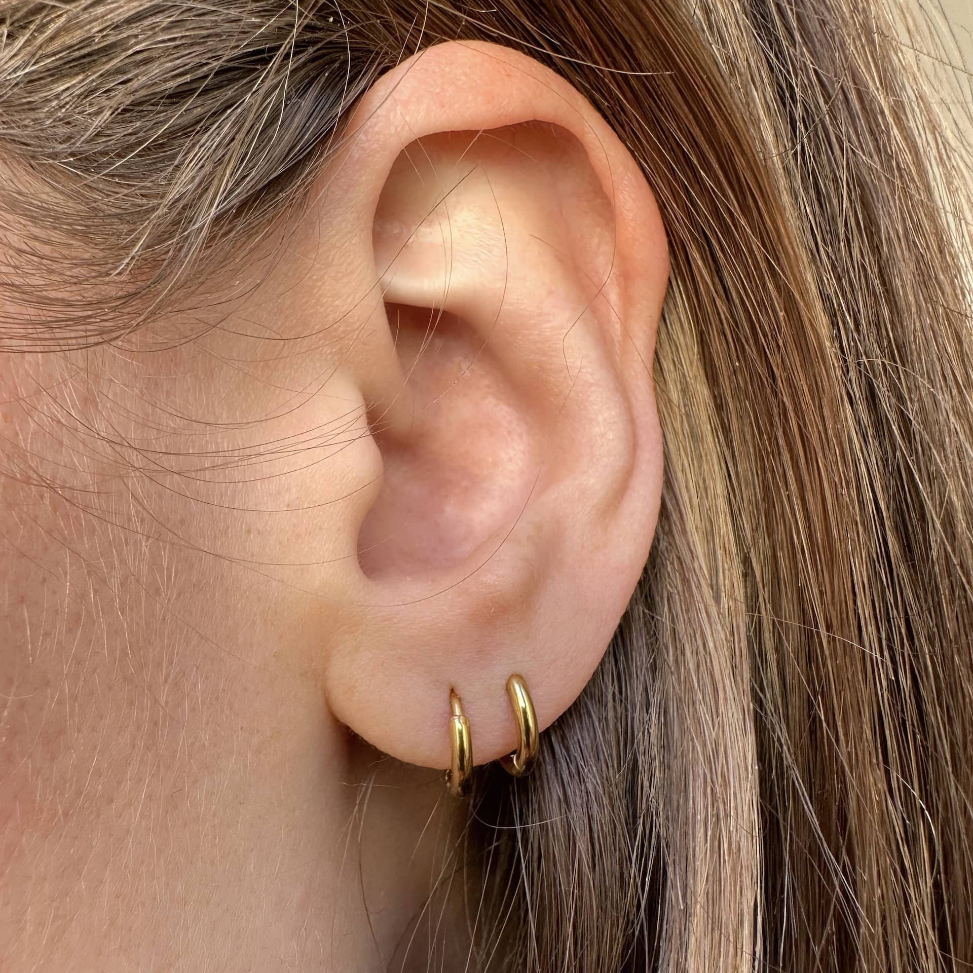 Mini Creolen in gold getragen im ersten und zweiten Ohrloch einer Frau