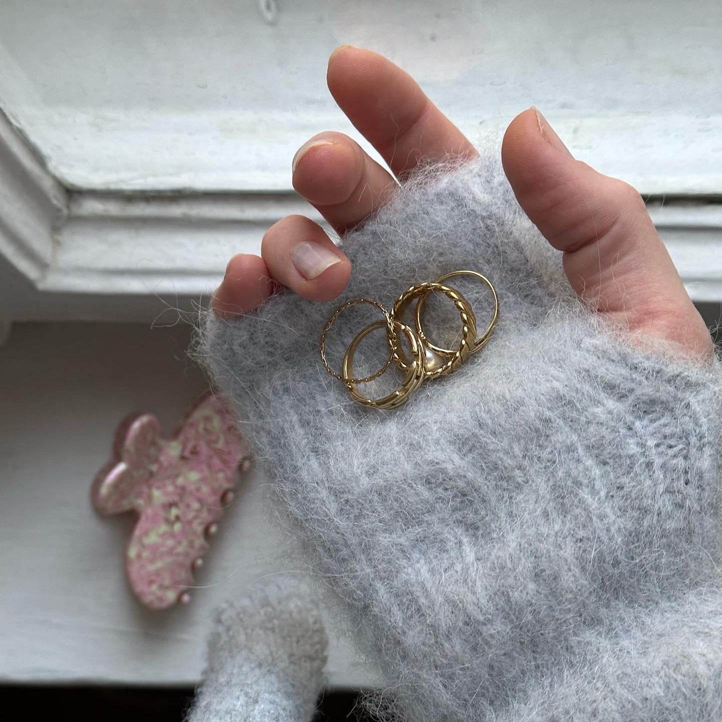 Hand, in der Ringe liegen mit pinker Haarspange im Hintergrund