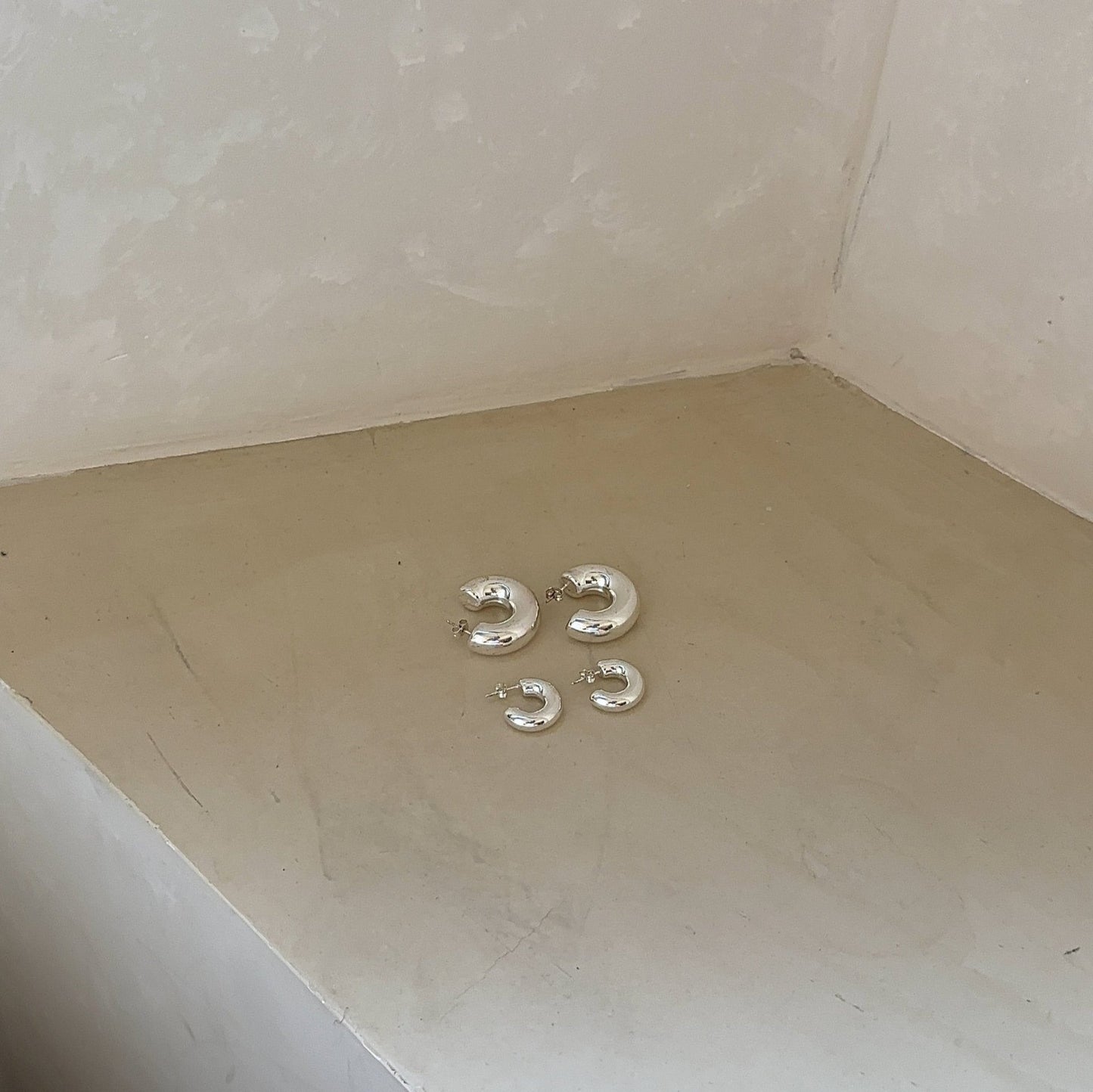 silver earring hoops in big and small on beige corner of the room