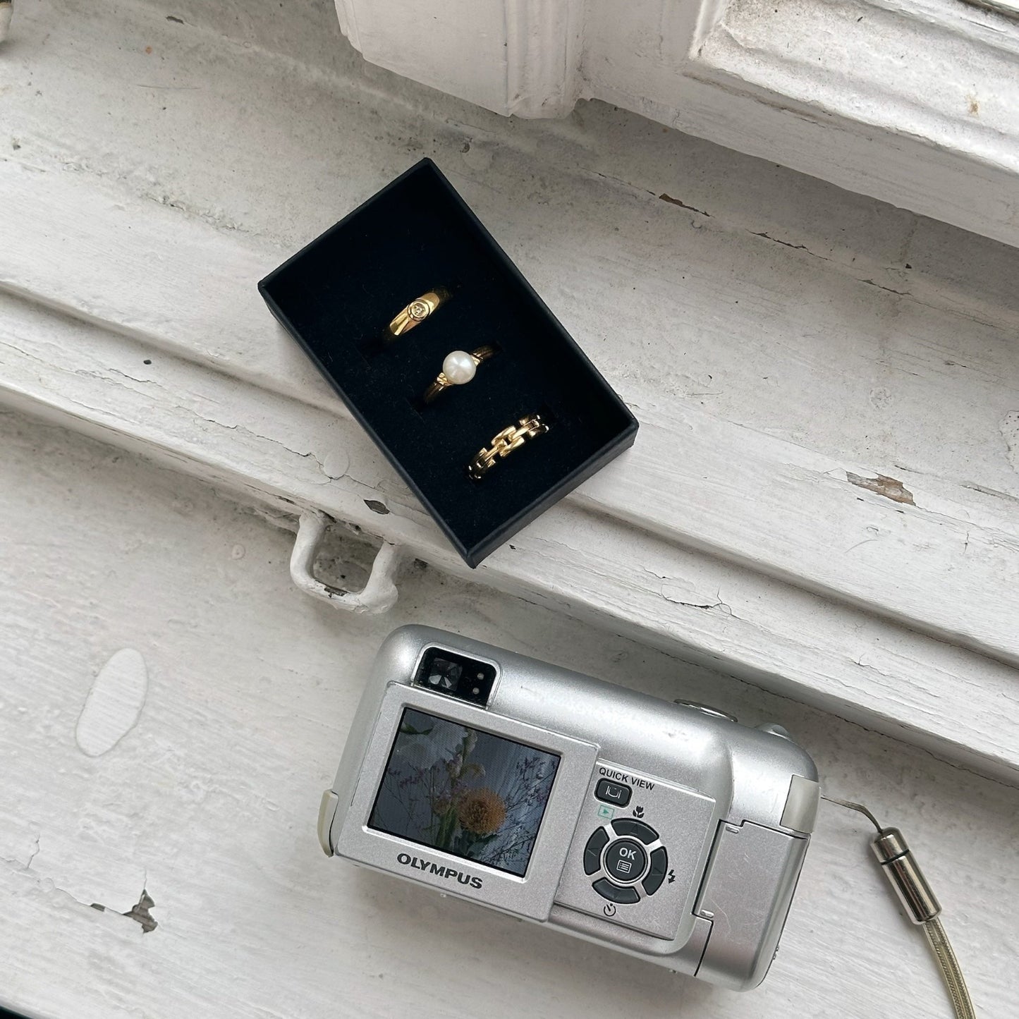 ring stack in jewelry box on white window frame next a silver digital camera