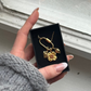 mix and match necklace with love letter, champagne flower and strawberry charm in jewelry box hold by a hand in fron of which wood and a glass window