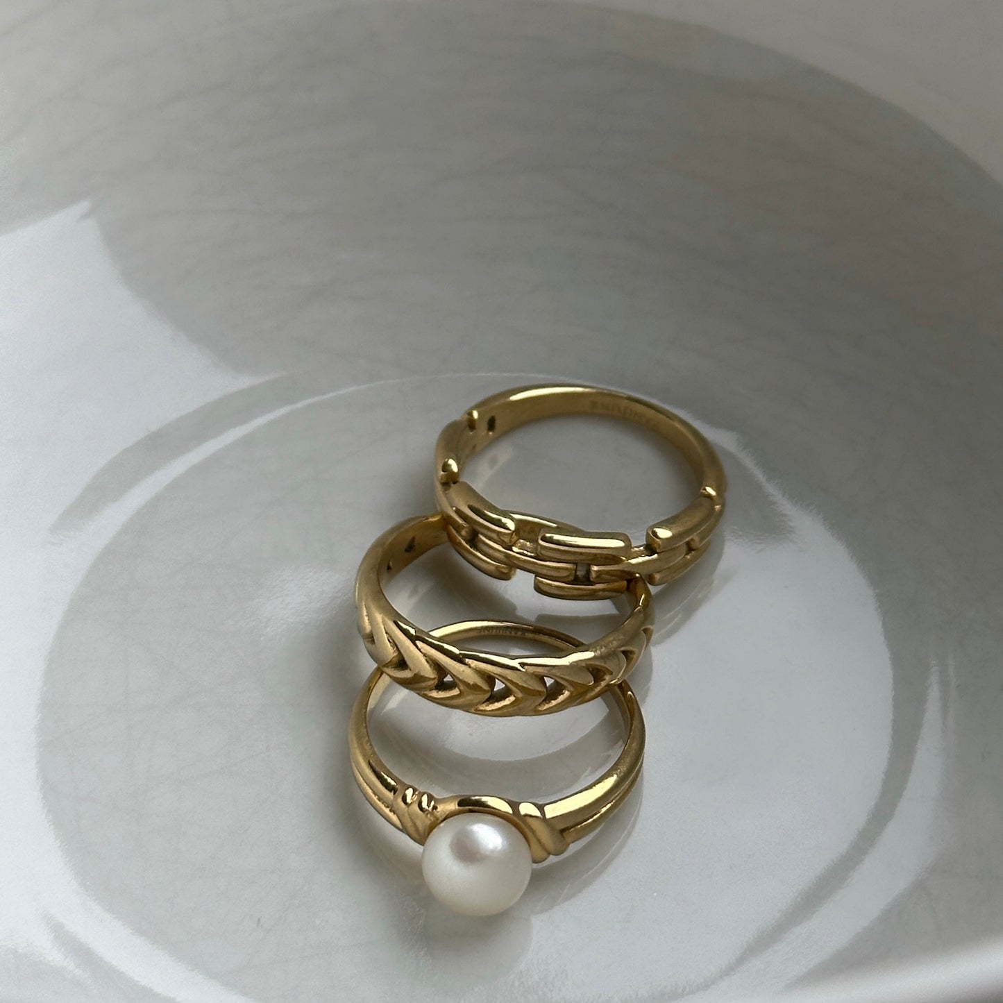Goldener Ring mit Süßwasserperle in weißer Keramikschale zusammen mit zwei weiteren Ringen in gold