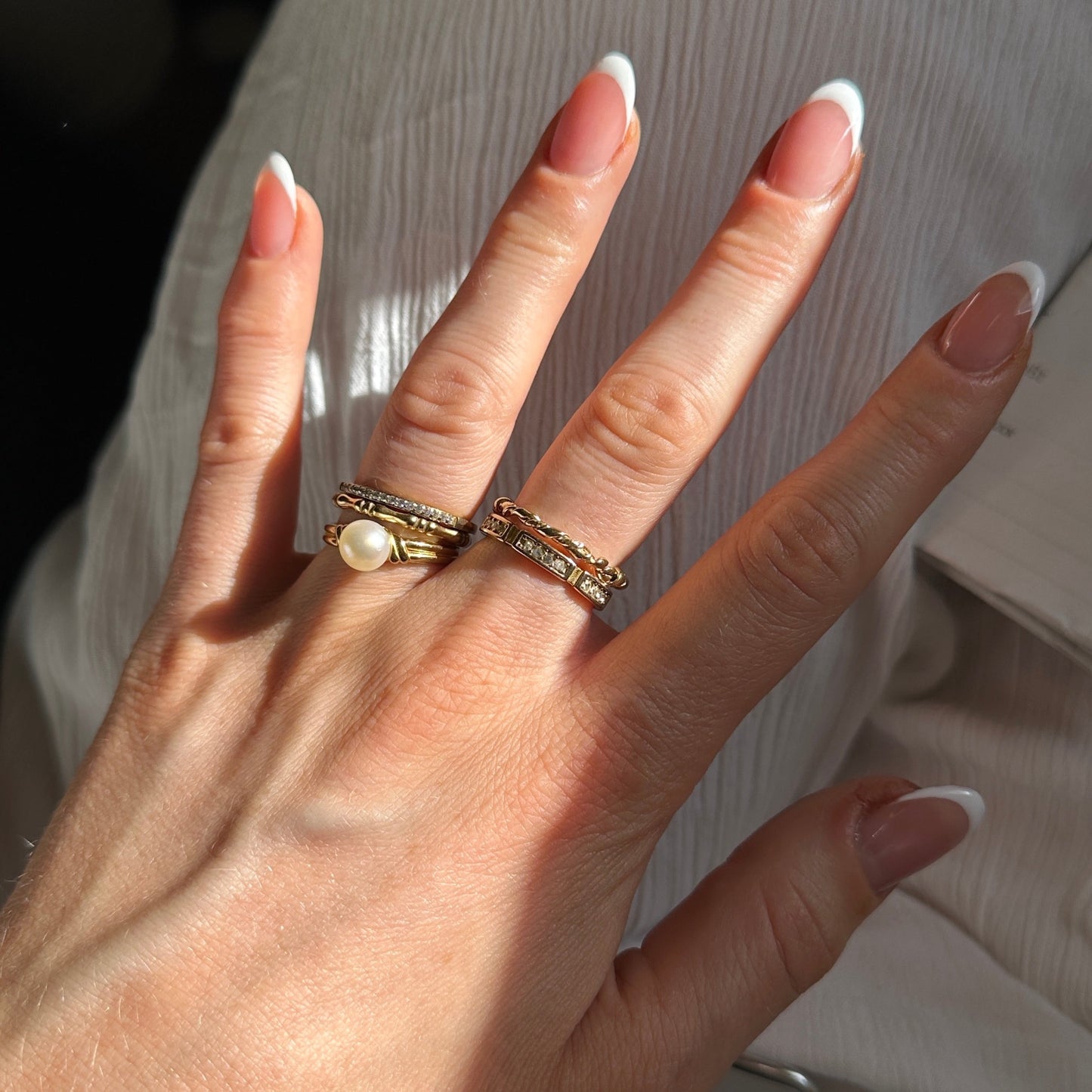 Goldener Ring mit Süßwasserperle getragen an Hand im Sonnenschein, zusammen mit weiteren goldenen Ringen