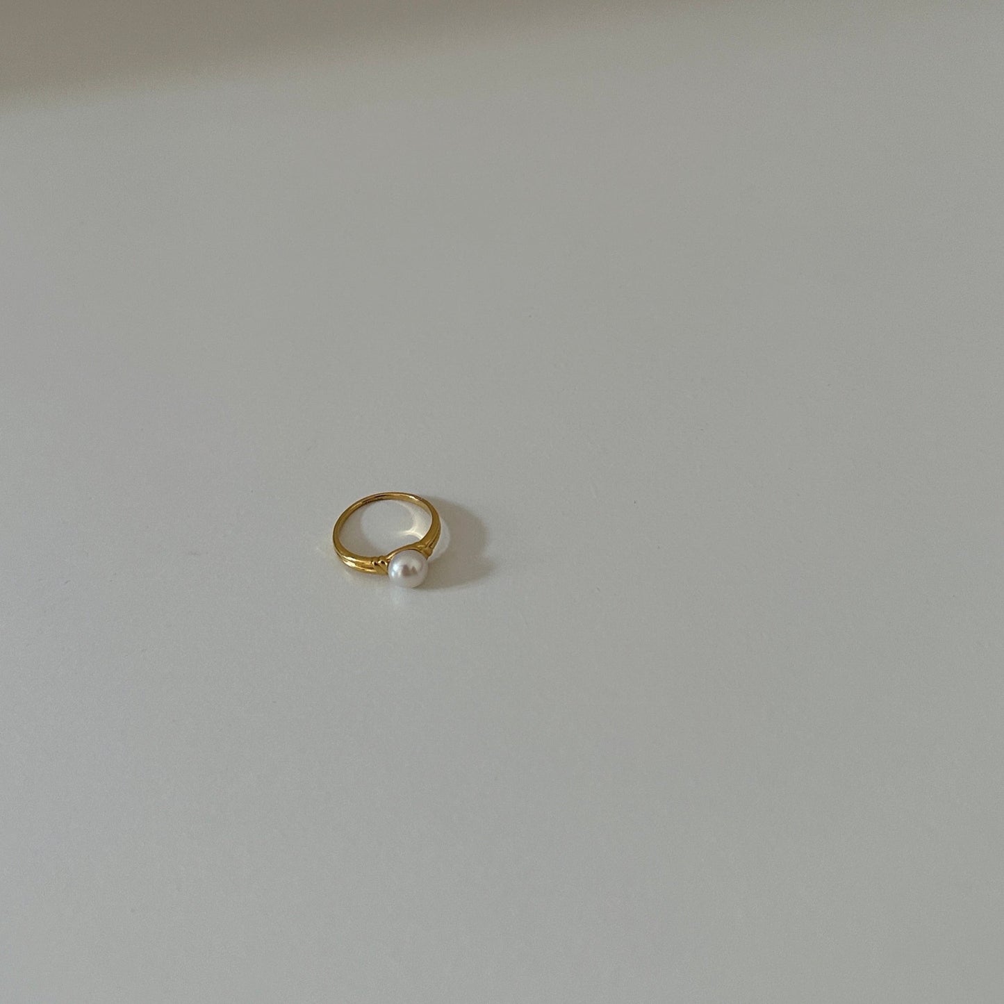 Goldener Ring mit Süßwasserperle in Weitaufnahme auf weißer Tischplatte